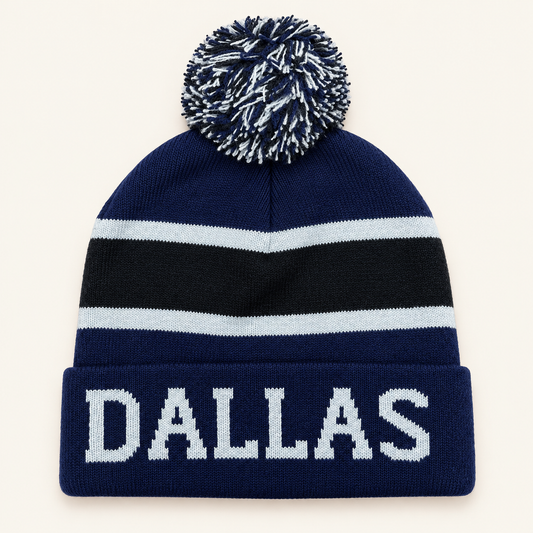 Navy Dallas pom-pom beanie with black and pale gray stripes on a warm off-white background.