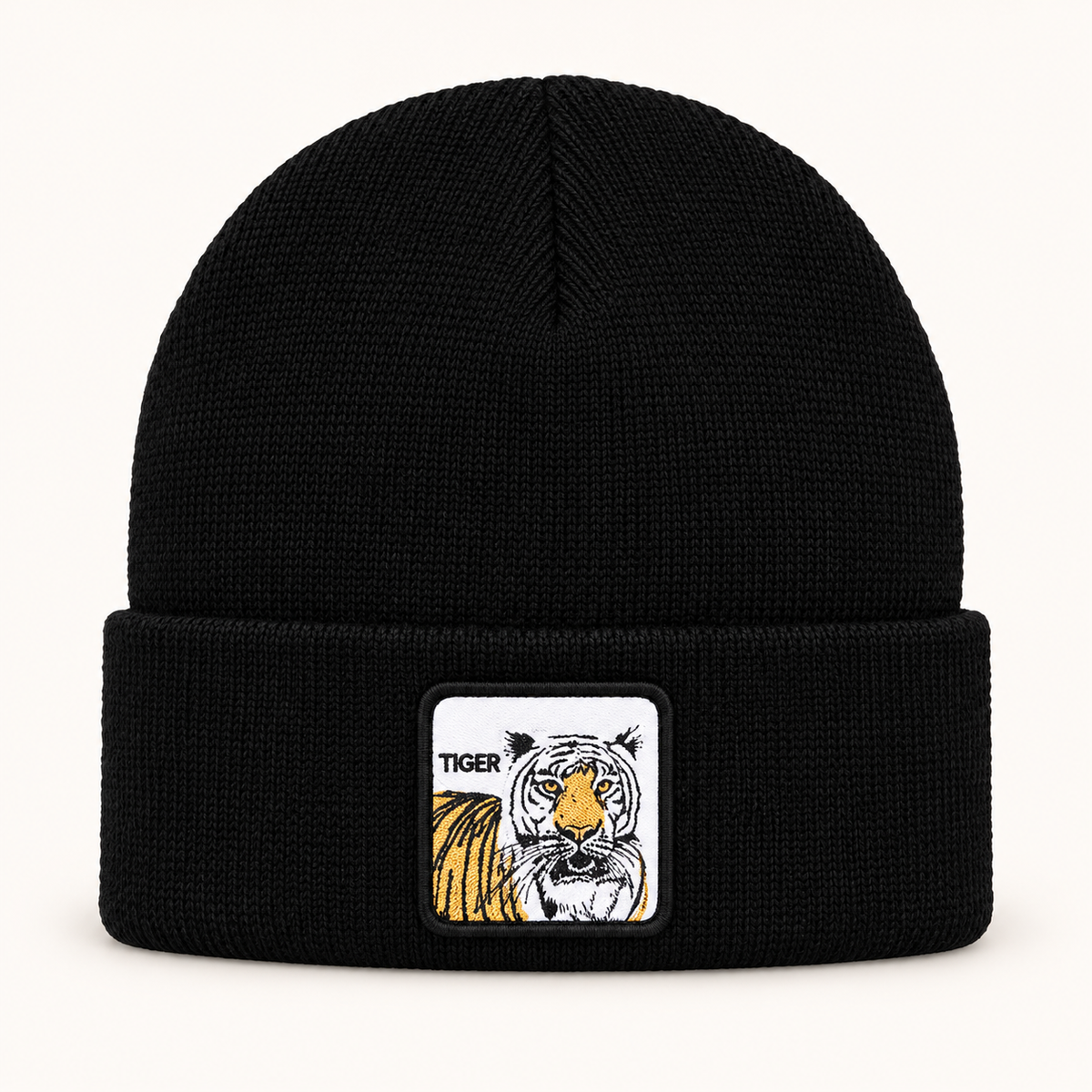 Black tiger-patch knit beanie, single hat on a clean off-white background.